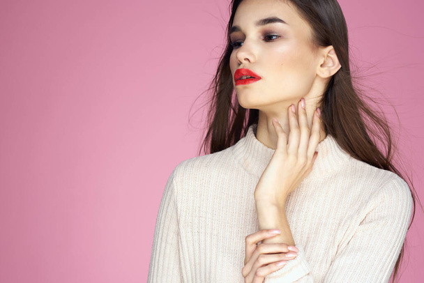 Pretty brunette in a white sweater red lips attractive look pink background - Фото, изображение
