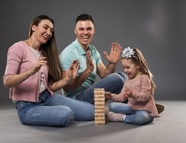 Happy young family with mother, father and little daughter, studio shot over gray background - Fotografie, Obrázek