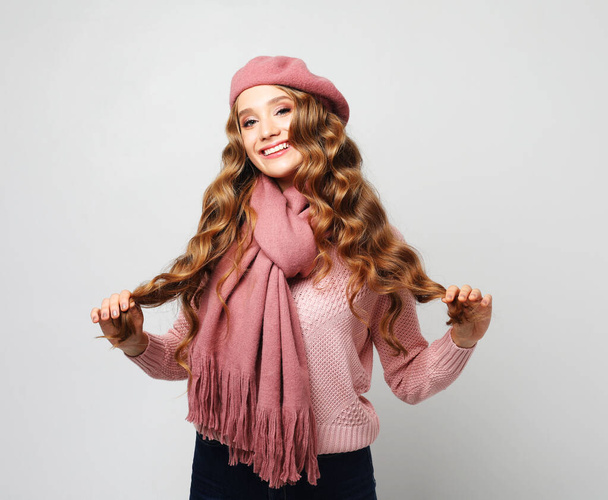 Smiling blonde looks at the camera. Young woman with curly hair wearing a pink T-shirt, scarf, and beret. - Zdjęcie, obraz