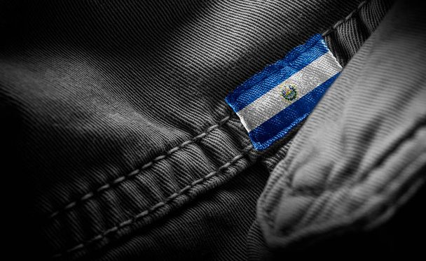 Etiqueta en la ropa oscura en la forma de la bandera del Salvador - Foto, Imagen