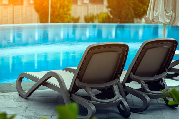 Ein Paar bequeme graue Liegestühle vor dem Hintergrund eines schönen, transparenten Pools und Hotels. Das Konzept eines erholsamen Badeurlaubs zu zweit - Foto, Bild