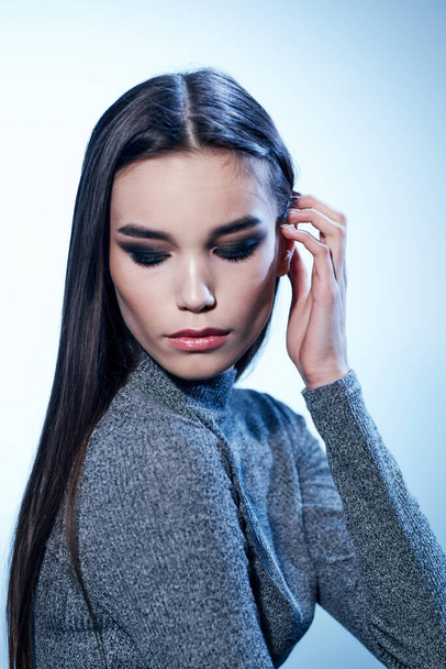 Portrait of an attractive woman on a light background in a gray sweater and makeup on her face - Foto, Imagen