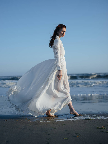 Encantadora mujer en un vestido de sol cerca del océano en la orilla de la playa modelo de pelo rojo - Foto, imagen