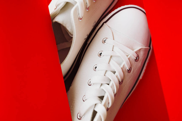white new clean sneakers with white laces on a rubber sole in a red paper background. - Photo, Image