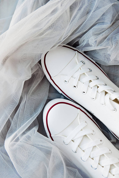 nuove scarpe da ginnastica bianche pulite con lacci bianchi su una suola di gomma su un tessuto di tulle grigio. una combinazione di scarpe sportive e abbigliamento formale. contenuto stile di abbigliamento. focus selettivo - Foto, immagini