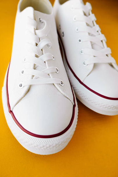 witte nieuwe clean sneakers met witte veters op een rubberen zool op een felgele achtergrond. selectieve focus - Foto, afbeelding
