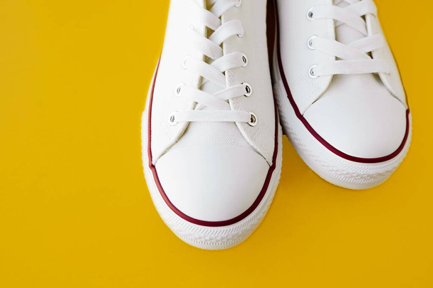 tênis limpos novos brancos com cadarços brancos em uma sola de borracha em um fundo amarelo brilhante. foco seletivo - Foto, Imagem