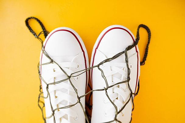 white clean sneakers in woven eco-friendly bag-string bag on bright yellow background. eco-friendly lifestyle of young people. wellness content. selective focus - Photo, Image