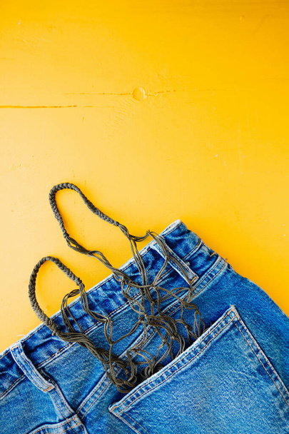 wicker eco-friendly string bag in the back pocket of jeans on bright yellow background. eco-friendly lifestyle of young people. wellness content. selective focus - Photo, Image
