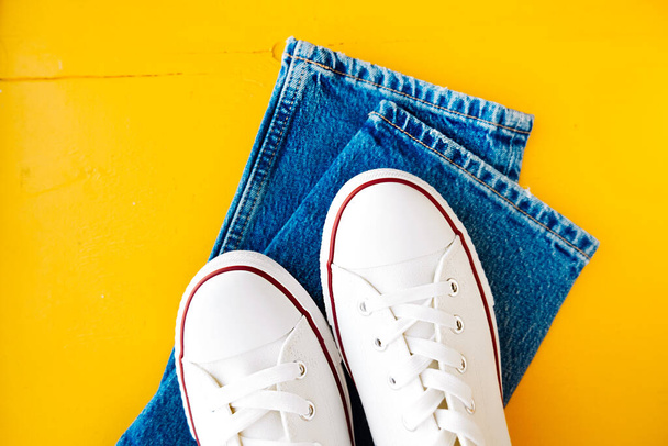 tênis limpos novos brancos com cadarços brancos em uma sola de borracha e calça azul em um fundo amarelo brilhante. conteúdo de roupa elegante. foco seletivo - Foto, Imagem