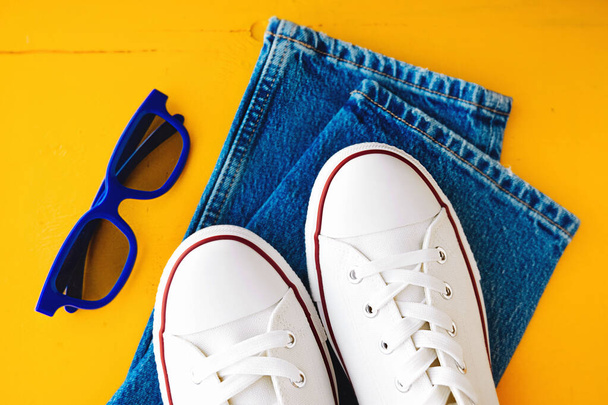 3D-Brille, weiße neue saubere Turnschuhe mit weißen Schnürsenkeln auf Gummisohle und blaue Jeans auf leuchtend gelbem Hintergrund. stilvolle Kleidung Inhalt. Selektiver Fokus - Foto, Bild
