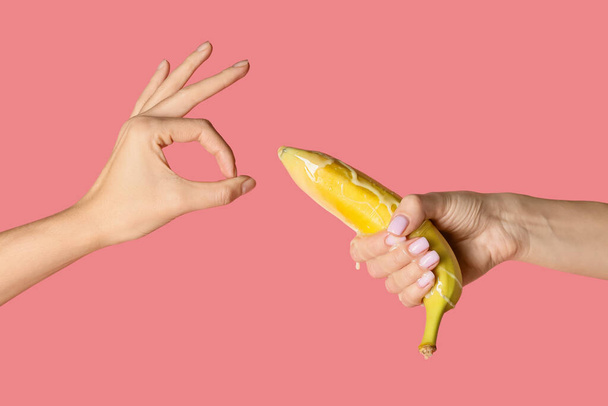 Frauenhände mit Banane im Kondom und mit Flüssigkeit auf farbigem Hintergrund. Erotisches Konzept - Foto, Bild
