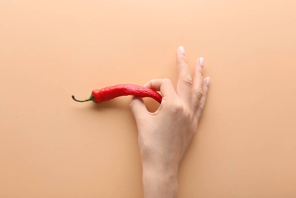 Female hand with chili pepper on color background. Erotic concept - Foto, afbeelding