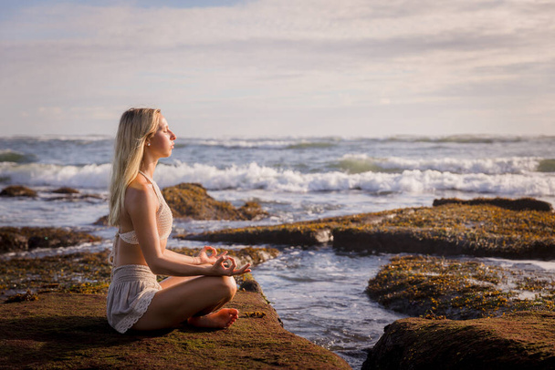 Женщина практикует йогу на пляже. Сидя в Падмасане, Лотос Поуз. Руки в гьянской грязи. Положительная энергия. Концепция здоровой жизни. Отдых на йоге. Принято. Вид на океан Пляж в Бали, Индонезия - Фото, изображение