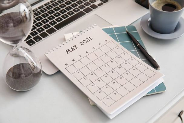 Kalendarz papierowy z laptopem, klepsydrą i papeterią na stole - Zdjęcie, obraz