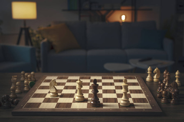 Chess game with pieces arranged on the board and living room interior in the background - Foto, Bild