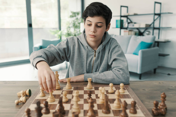 Intelligent boy playing chess at home, he is moving a piece on the chessboard - Photo, Image