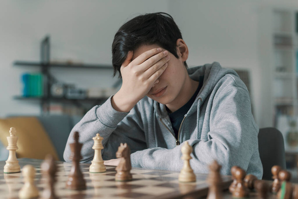 Boy playing chess and losing the game, he is disappointed and covering his face with the hand - Фото, зображення