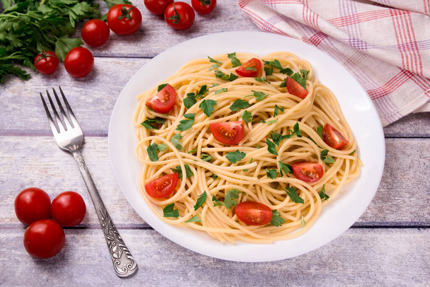 Tészta spagetti cseresznye paradicsommal, sült kolbász és petrezselyem fehér tányérral, könnyű háttérrel, finom, természetes. - Fotó, kép