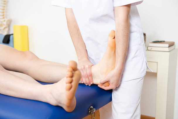 Closeup view of a physiotherapist treating the foot and ankle mobility of a sportive patient. - Foto, afbeelding