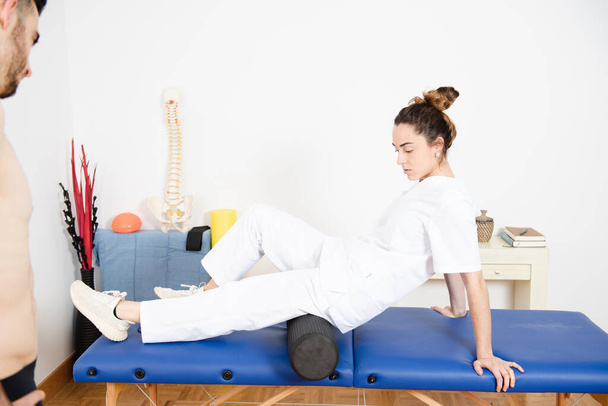 Physiotherapist explaining a self-massage technique using a foam roller to a patient. - Photo, Image