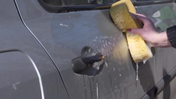 Μια γυναίκα πλένει το σώμα ενός αυτοκινήτου με ένα σφουγγάρι. - Πλάνα, βίντεο