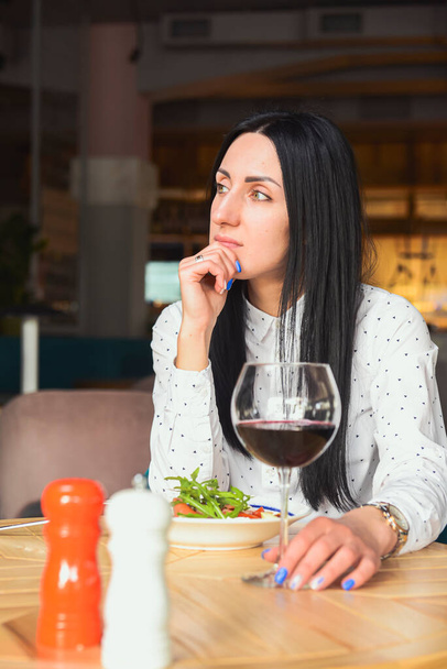 Young attractive woman having a healthy lunch in restaurant. Caucasian female with black hair dining. Eating out concept, eating alone in restaurant due to Covid-19 pandemic. - Φωτογραφία, εικόνα