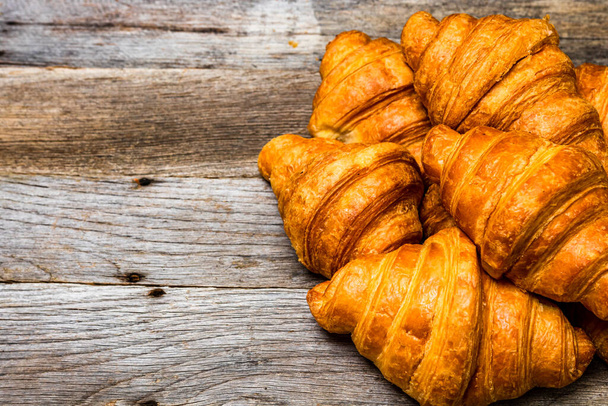 A closeup shot of delicious and fresh croissants on a wooden surface - copy space - Fotoğraf, Görsel