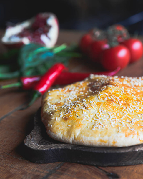 Khachapuri with cheese served on a wooden board over dark rustic wooden table. Traditional Georgian cuisine concept. Selective focus, blurred background. - Foto, Imagen