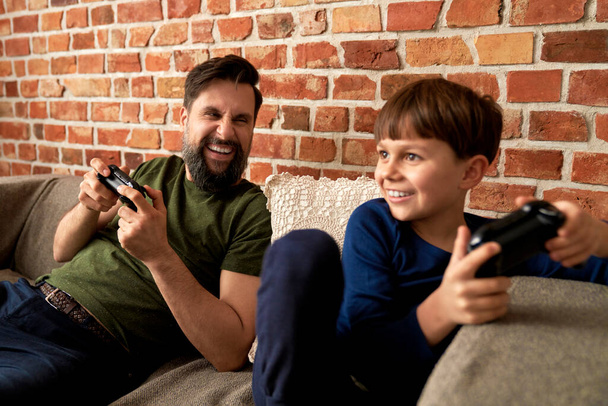 Πατέρας και γιος διασκεδάζουν κατά τη διάρκεια του παιχνιδιού στο σπίτι                                - Φωτογραφία, εικόνα