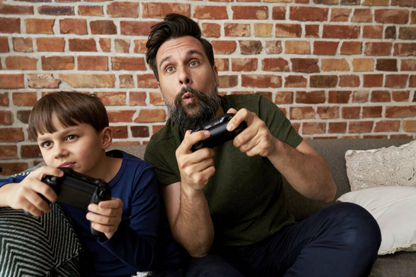 Padre e hijo enfocados mientras juegan videojuegos                                - Foto, Imagen
