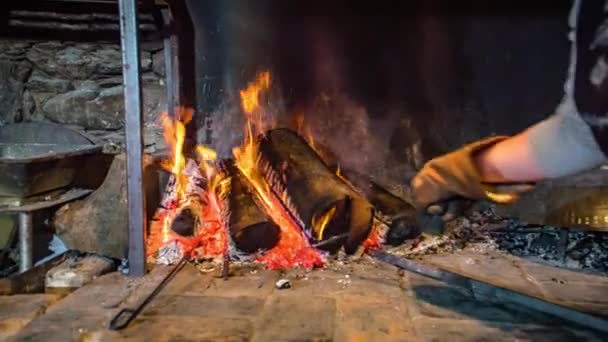 Movimiento lento de una mujer con guantes calentando un palo de hierro cerca de las cenizas ardientes de un horno de wod - Imágenes, Vídeo