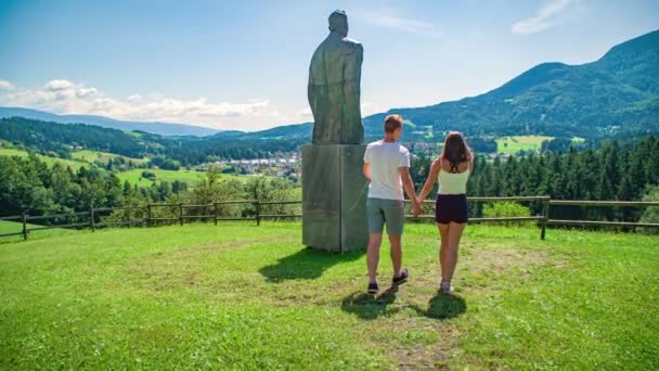 Young lovebirds hold hands and walk across a park to enjoy a scenic view of a village - Záběry, video