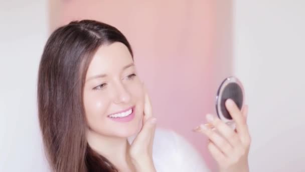 Kobieta patrząc na kompaktowe lustro i bada jej skórę, dotykając twarzy i uśmiechnięty, długa fryzura i naturalny makijaż, portret twarzy piękna modelki jako produktu kosmetycznego i komercyjnej pielęgnacji skóry - Materiał filmowy, wideo