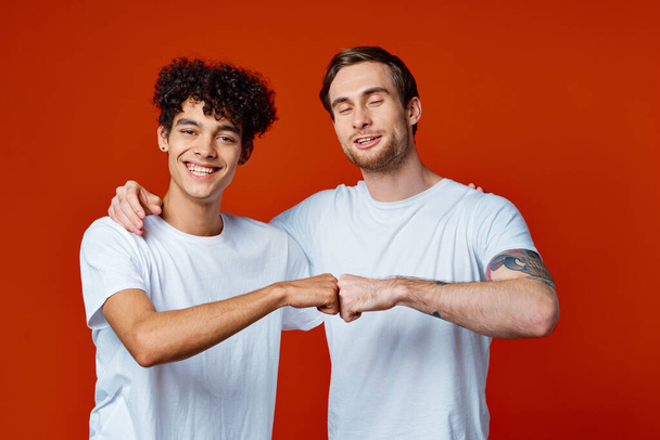 zwei Freunde in weißen T-Shirts umarmen Kommunikation roten Hintergrund - Foto, Bild