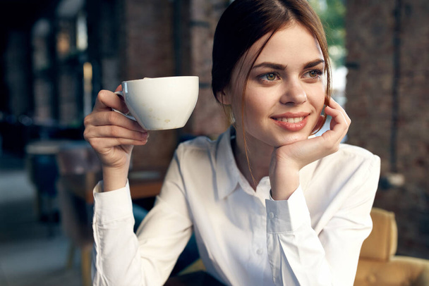 pretty business woman in white shirt sits in a cafe with a cup of coffee. High quality photo - Foto, afbeelding
