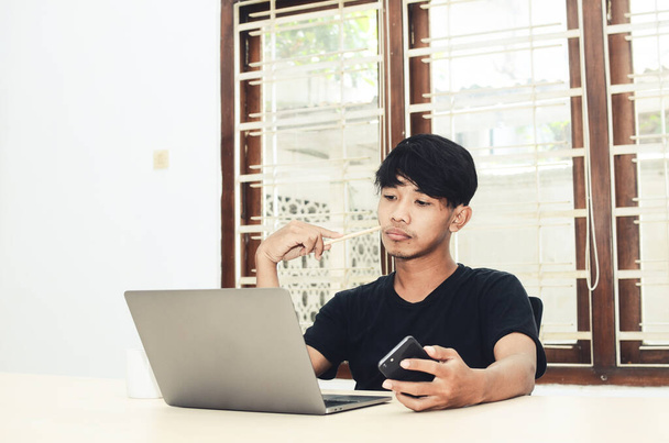 Mężczyzna w czarnej azjatyckiej koszulce siedział przed laptopem ze smutnym wyrazem twarzy. - Zdjęcie, obraz