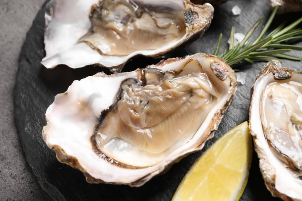 Delicious fresh oysters with lemon served on grey table, closeup - Fotoğraf, Görsel