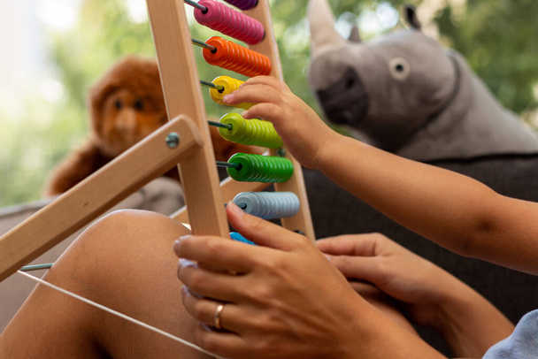 Close up captura de mãos de mãe e criança brincando com ábaco colorido de madeira com brinquedos de pelúcia no quadro - Foto, Imagem