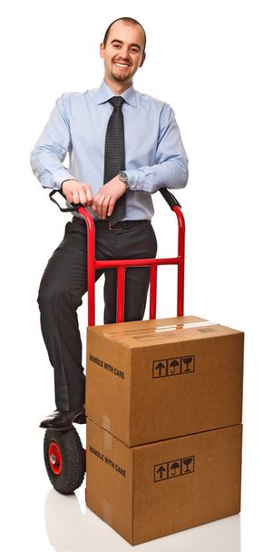 Smiling businessman with red handtruck and boxes - Фото, изображение