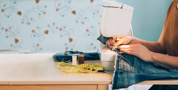 Una sarta donna lavora alla macchina da cucire cuce riutilizza tessuto da vecchi vestiti di denim - Foto, immagini