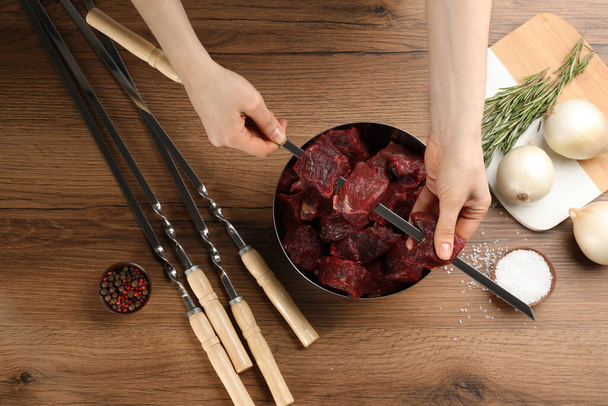 Woman stringing marinated meat on skewer at wooden table, top view - Foto, Imagem