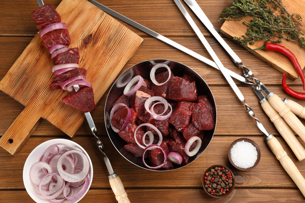 Flat lay composition with metal skewers and bowl of raw meat on wooden table - Zdjęcie, obraz