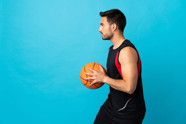 Молодой красивый мужчина на голубом фоне играет в баскетбол - Фото, изображение