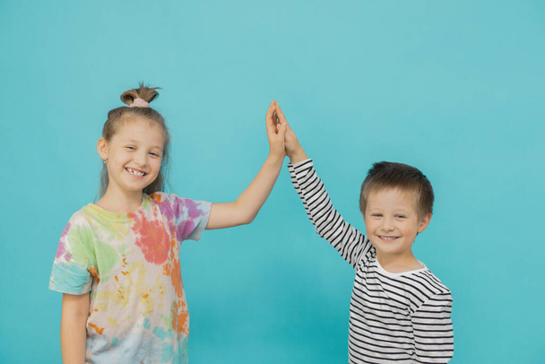 A girl and a boy of Caucasian appearance hold hands and look at the camera on a blue background. Teamwork, friendship and victory concept - Fotografie, Obrázek
