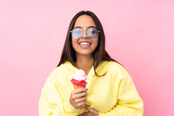Young brunette girl holding a cornet ice cream over isolated pink background smiling a lot - 写真・画像