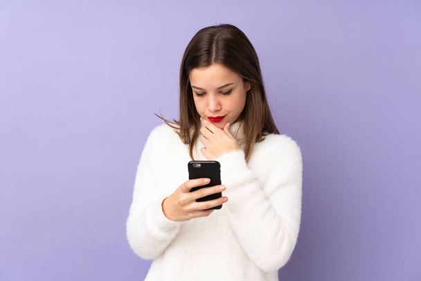 Teenager Mädchen isoliert auf lila Hintergrund denken und eine Nachricht senden - Foto, Bild