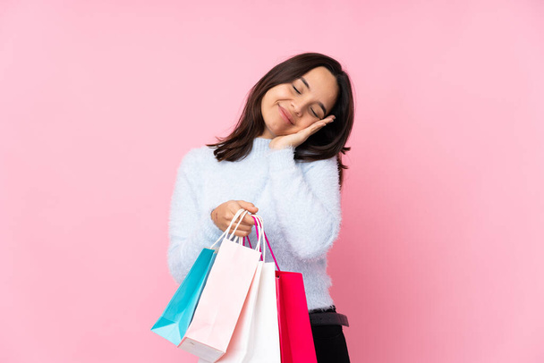 Young woman with shopping bag over isolated pink background making sleep gesture in dorable expression - Photo, Image