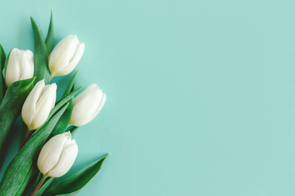 Zarte weiße Tulpen auf pastelltürkisfarbenem Hintergrund. Grußkarte zum Frauentag. Flach lag er. Platz für Text.  - Foto, Bild