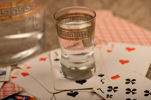 Jugando a las cartas y un vaso de vodka en una mesa cubierta con arpillera gruesa. Primer plano, enfoque selectivo. - Foto, imagen